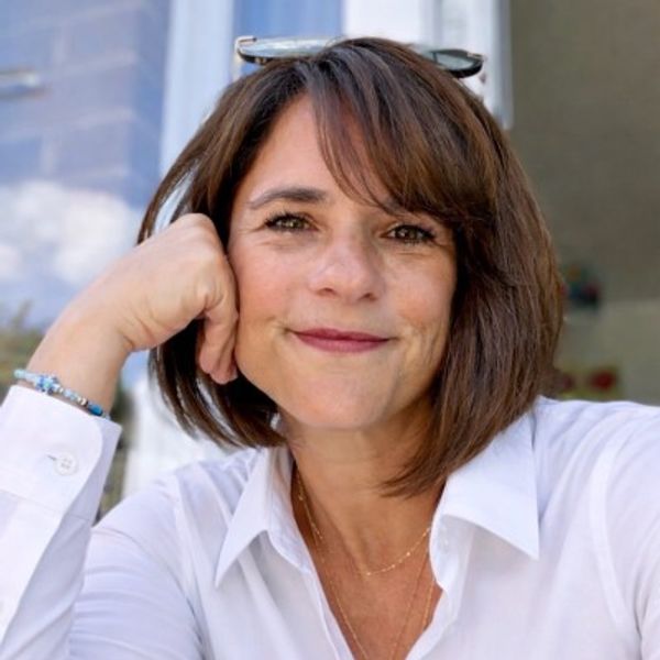 Smiling woman with short brown hair in a white shirt, resting her face on her hand.