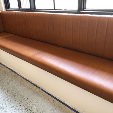 Long brown leather bench seating by windows in a modern space.
