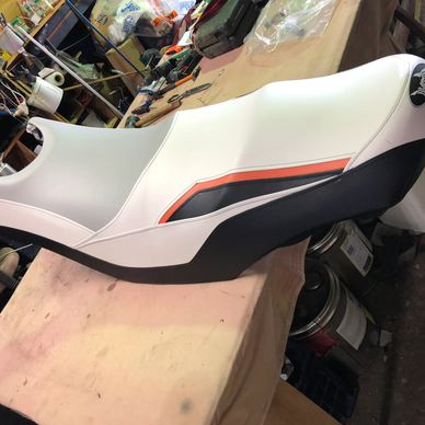 White and black motorcycle seat with red and black accents on a workbench.