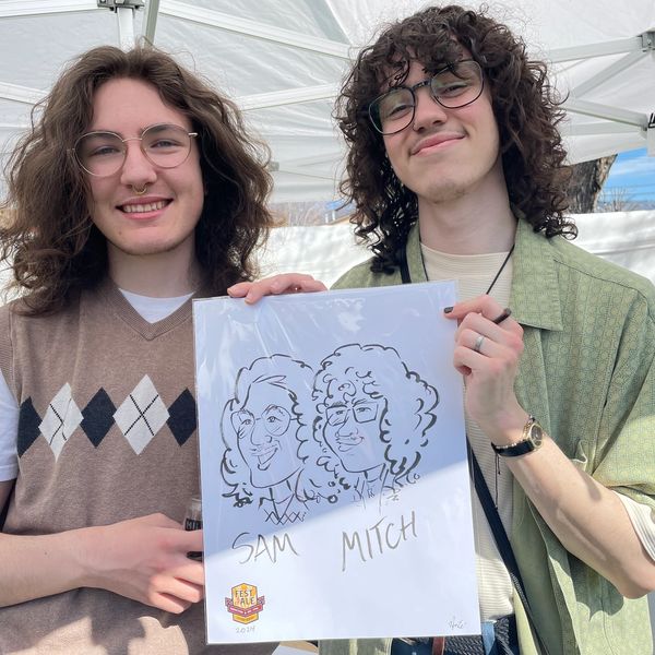 Two smiling young men holding a caricature drawing.
