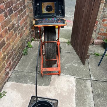 A sewer inspection camera setup with a monitor and cable inserted into a manhole.
