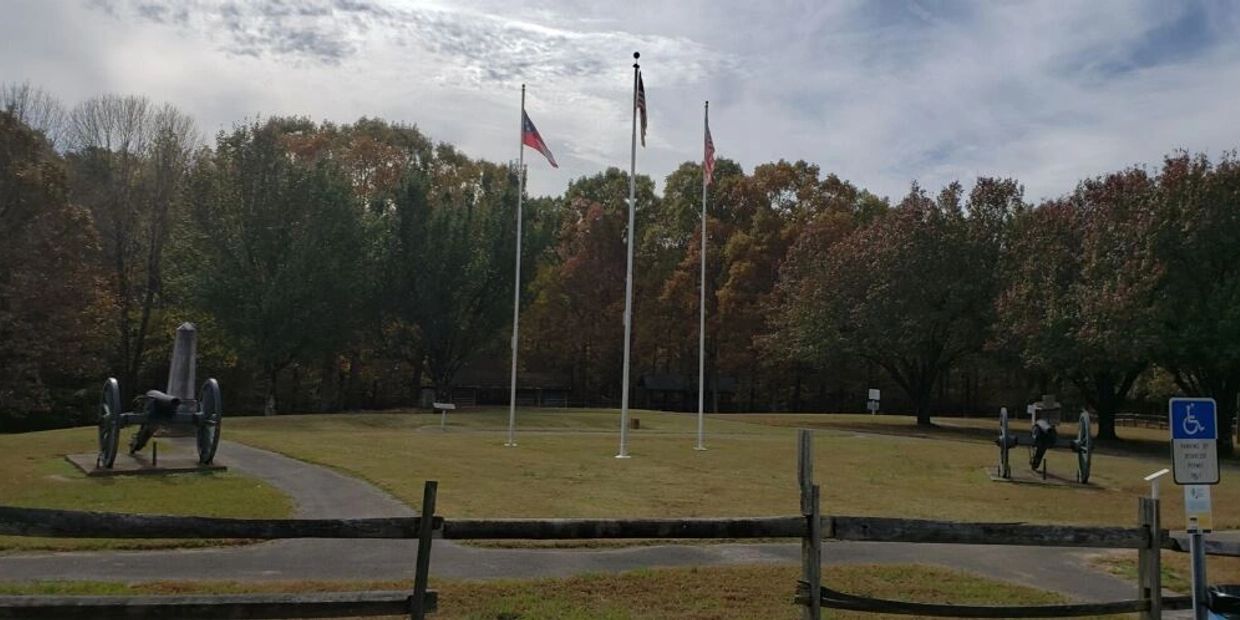 Three flags and cannons in a small park surrounded by trees.
