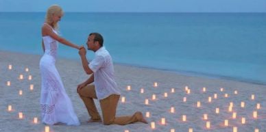 A man proposes to a woman on a candlelit beach at dusk.