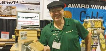Smiling vendor at a trade show booth with vintage electronics and promotional signs.