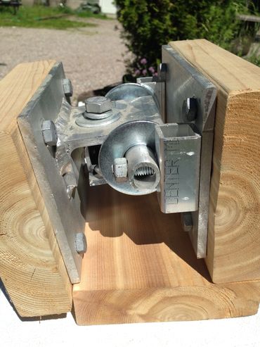 Metal hinge mechanism mounted between two wooden blocks outdoors.