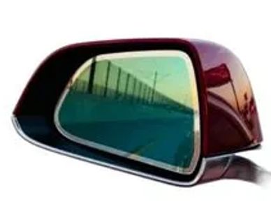 Maroon car side mirror reflecting a road and fence.