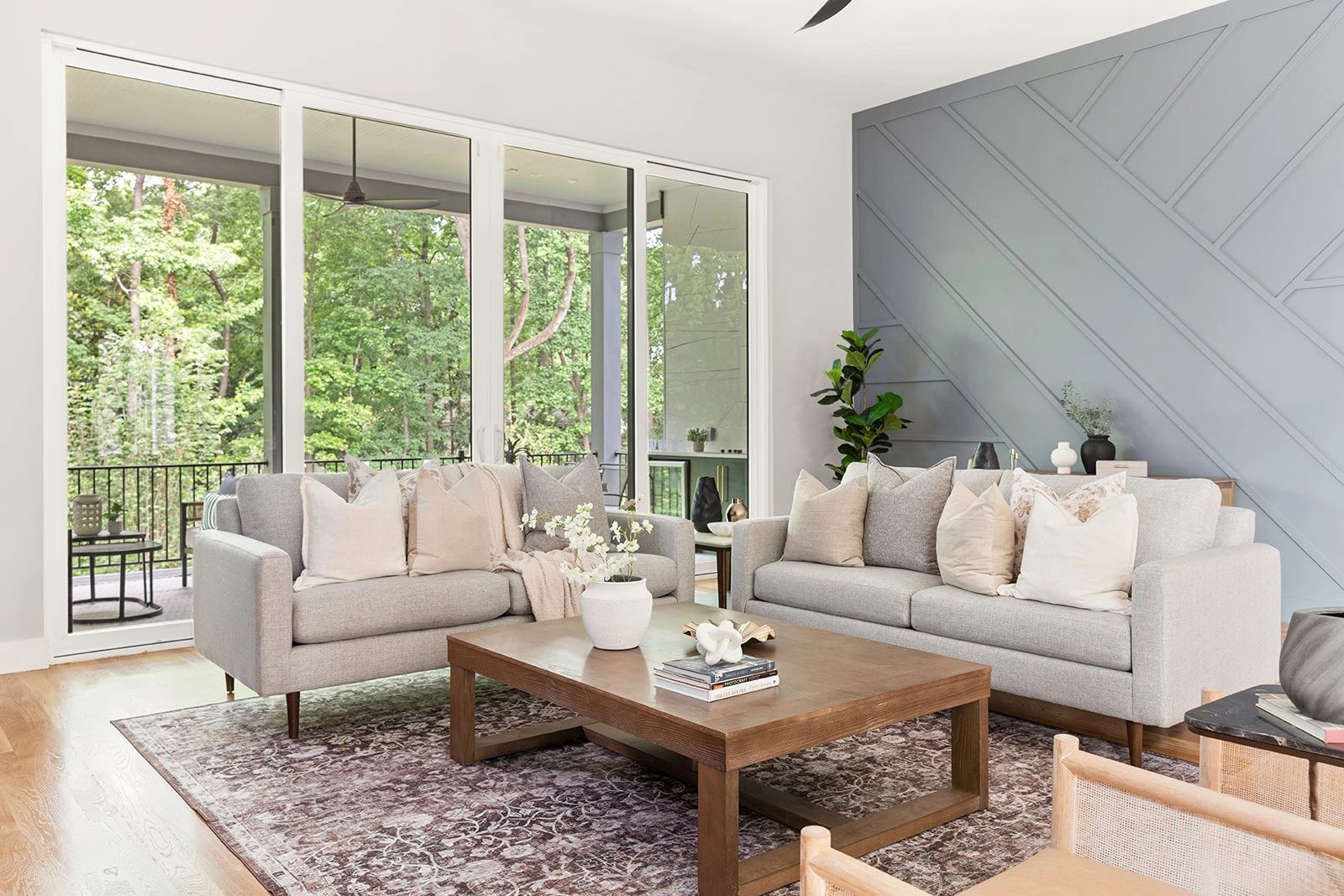 Modern living room with gray sofas, wooden coffee table, and large windows overlooking greenery.