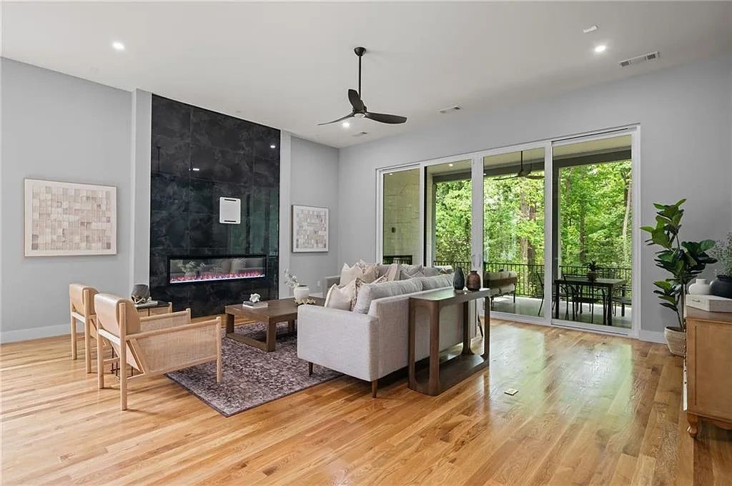 Modern living room with wooden floor, gray sofa, black fireplace, and large glass doors opening to a green outdoor space.