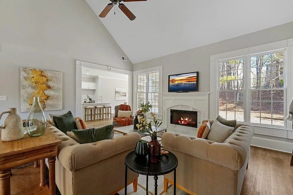 Cozy living room with beige sofas, a fireplace, and large windows letting in natural light.