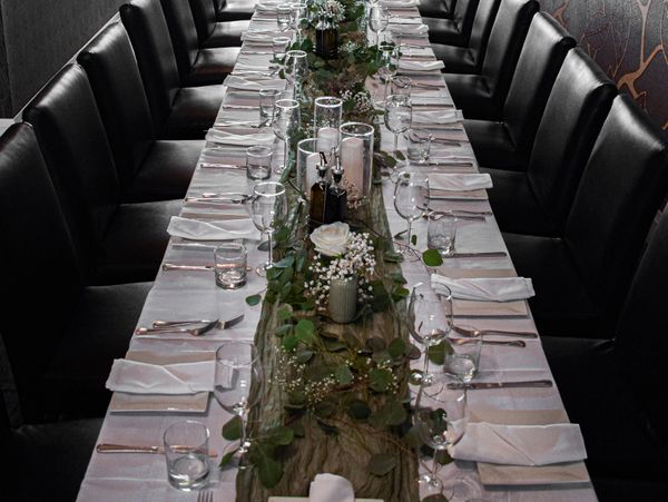Elegant long dining table set with white napkins and greenery centerpiece.
