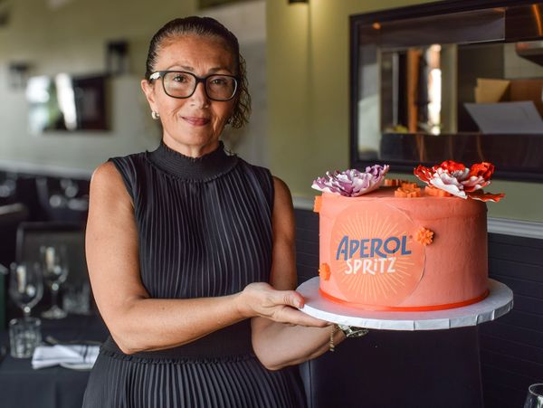 Woman holding an orange Aperol Spritz cake with floral decorations.