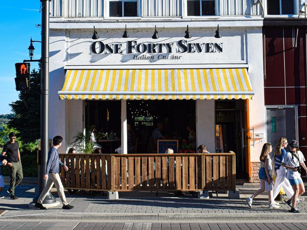 People walk past a restaurant named One Forty Seven with a yellow-striped awning.
