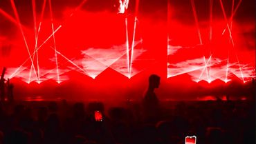A concert with red lighting and lasers illuminating pyramids on stage.
