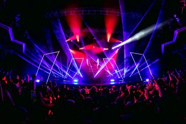 Vibrant light show at a crowded concert stage with colorful beams and geometric patterns.