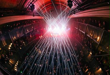Laser lights illuminate a crowded concert venue with an energetic atmosphere.