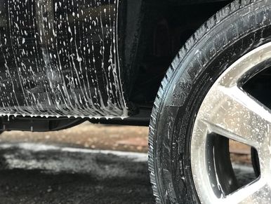 Car tire and side panel covered in soap suds during a wash.
