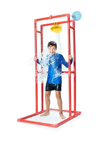 A boy stands under a playful water bucket dumping water on him.