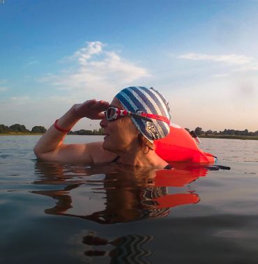 Person swimming with goggles and cap in a lake.