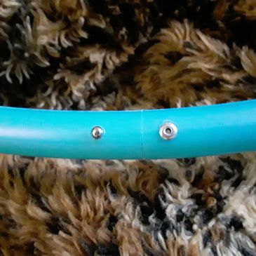 Close-up of a blue plastic tube with metal bolts on a textured carpet.