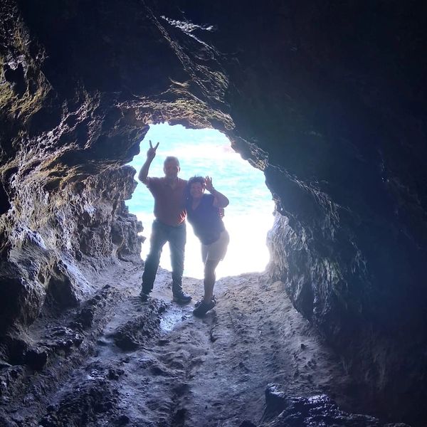 Two people posing inside a rocky cave with ocean light behind them.