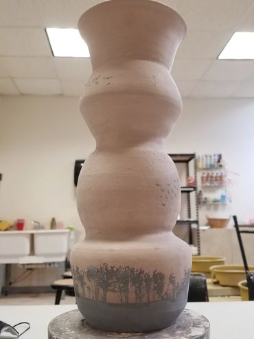 Tall, unglazed ceramic vase with a nature-inspired design at the base.
