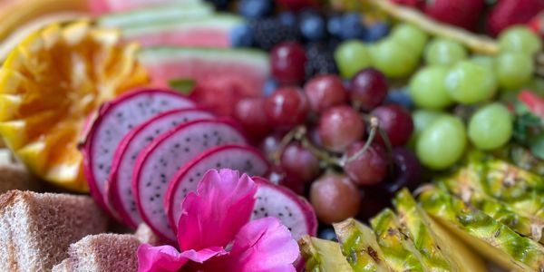 Colorful fruit and cheese platter with crackers and a pink flower decoration.