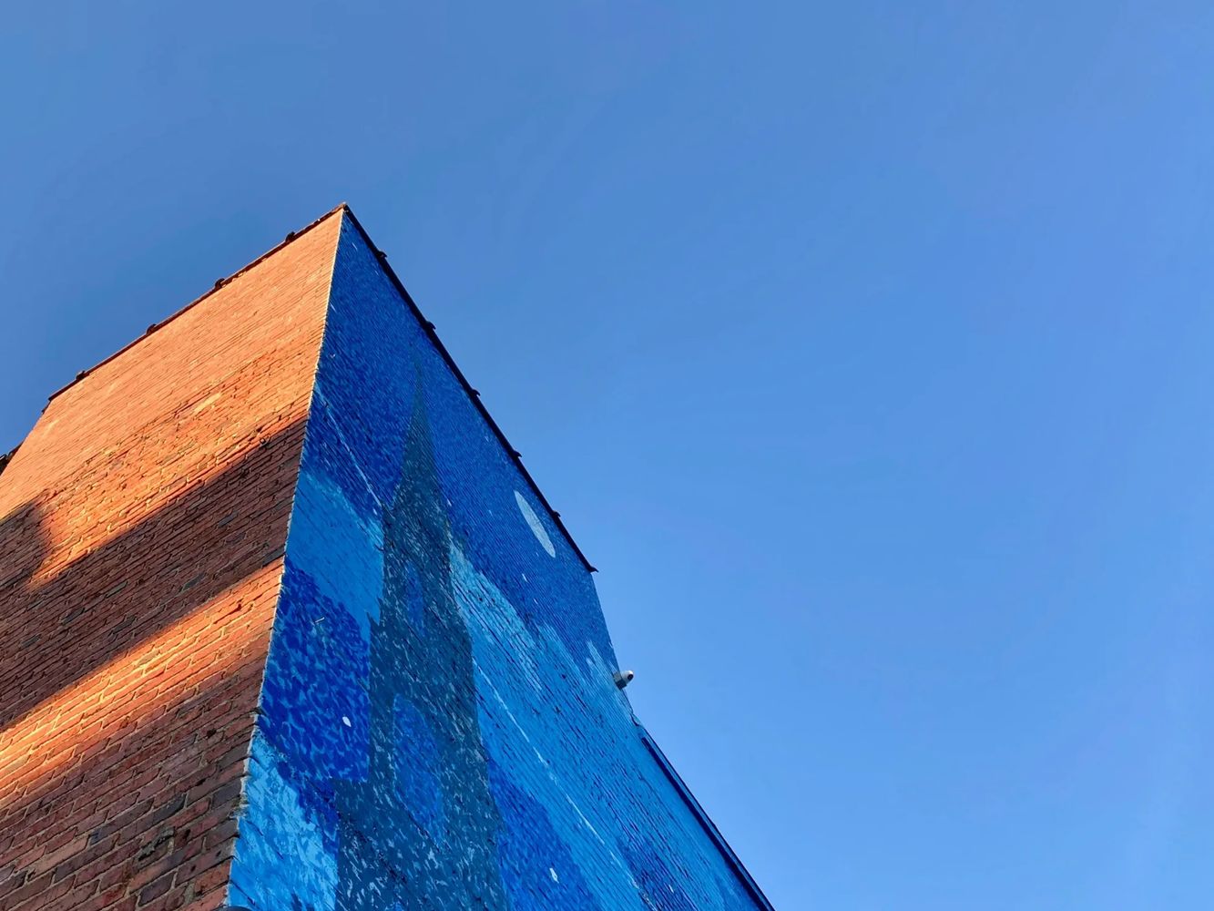 Brick building with a blue mural against a clear sky.