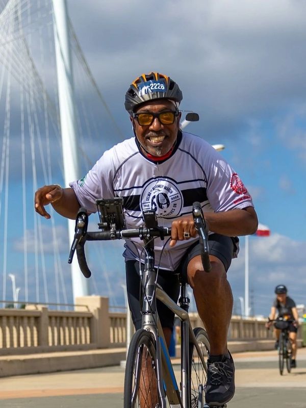 Man riding bicycle wearing helmet and sunglasses, smiling.