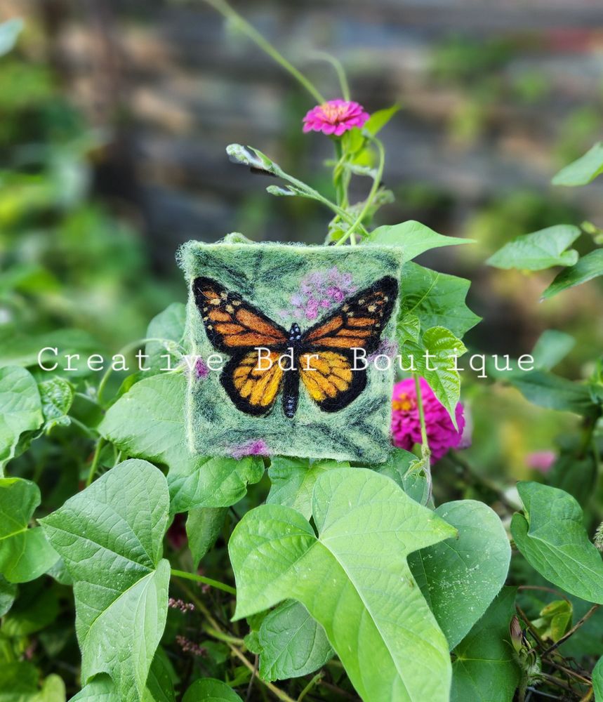 Felt butterfly artwork on green leaves with pink flowers.
