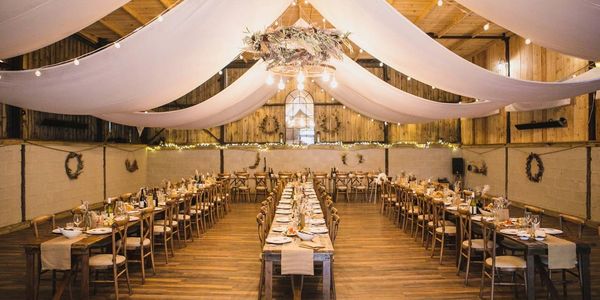 Elegant rustic dining hall decorated for an event with draped ceilings and wooden tables.