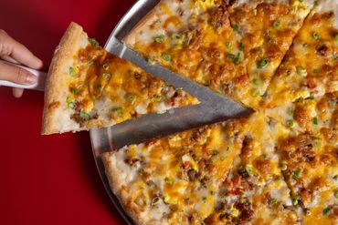 Hand picking a slice of cheesy breakfast pizza with sausage and green onions.