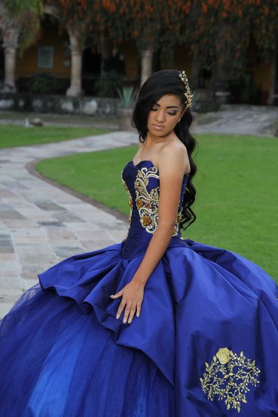 Young woman in an elegant royal blue ball gown with gold embroidery.