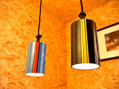 Two modern pendant lamps with colorful stripes hang against a textured wooden wall.
