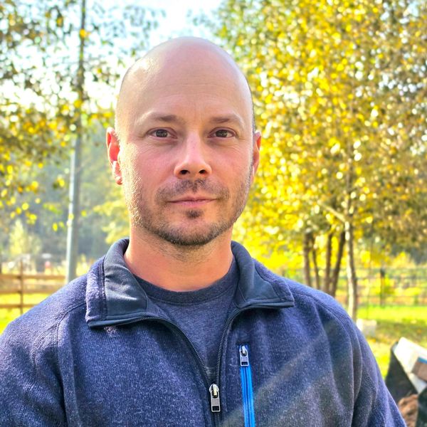 Man in a blue jacket outdoors with trees in the background.