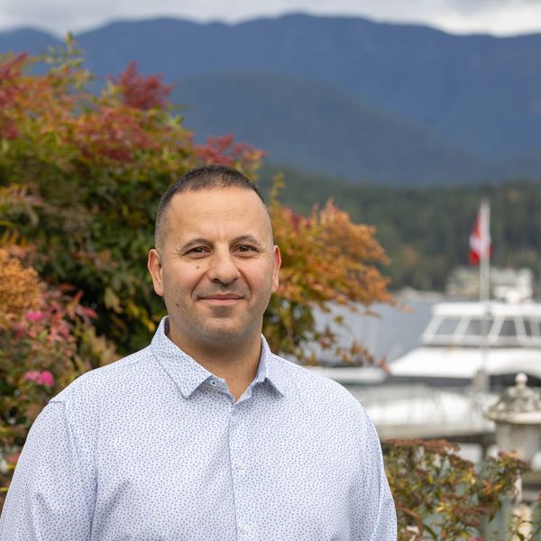 Man standing outdoors with mountains and a marina in the background.
