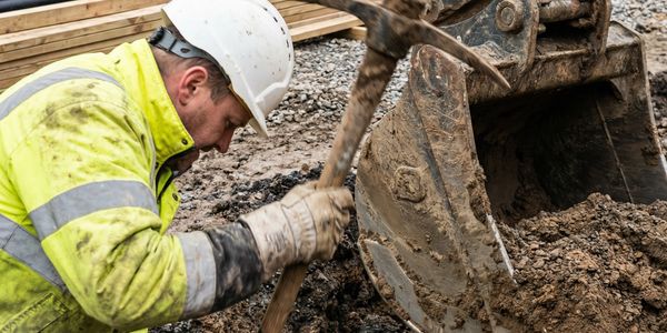 Construction worker digging with a pickaxe near excavator.