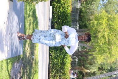 A woman in a white top and floral skirt standing outdoors on a sunny day.