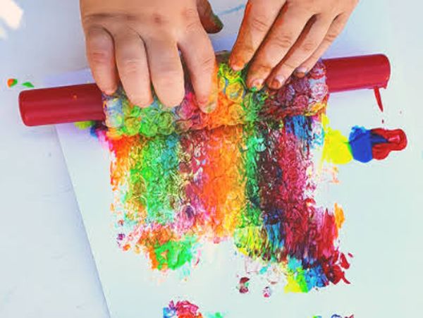 Child's hands rolling colorful paint on paper using bubble wrap and a rolling pin.