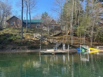 A lakeside cabin with a dock and paddle boats on a clear day.