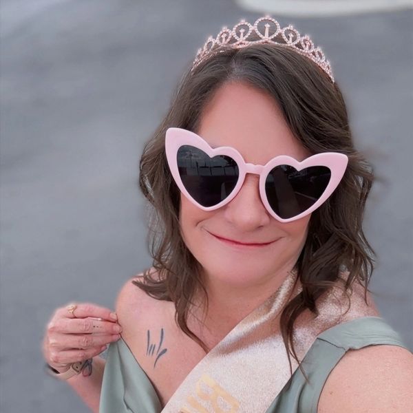 Woman wearing heart-shaped sunglasses and a tiara with a sash.