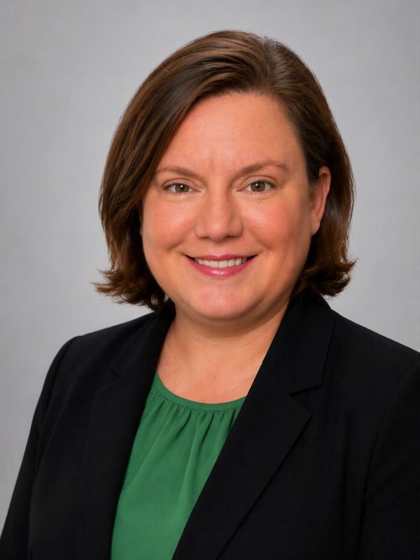 Smiling woman in green shirt and black blazer.