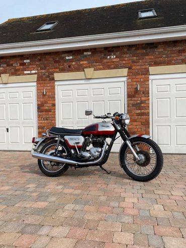 Classic motorcycle parked on a brick driveway in front of white garage doors.