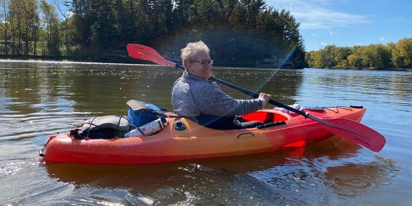 Person kayaking on a calm lake with blue sky.