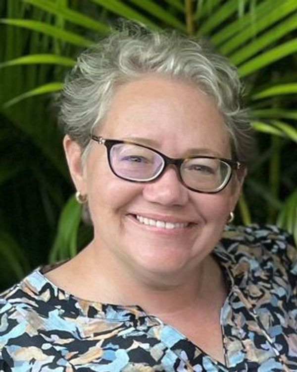 Smiling woman with short gray hair and glasses.
