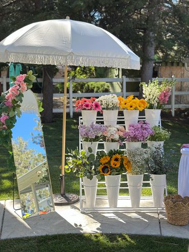 Outdoor flower display with a white umbrella and mirror.