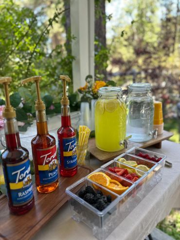 A colorful outdoor drink station with syrups, fruit, and refreshing beverages.