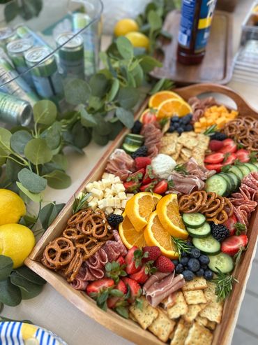 A vibrant charcuterie board with fruits, pretzels, crackers, and meats.