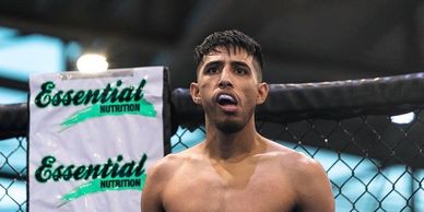 A focused male mixed martial artist stands in a cage with a mouthguard.