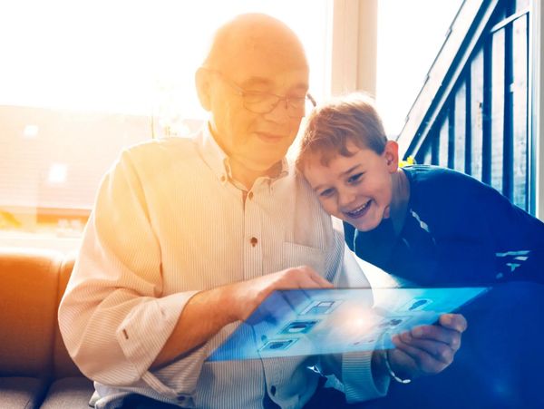 Grandfather and grandson joyfully using a futuristic transparent tablet together.