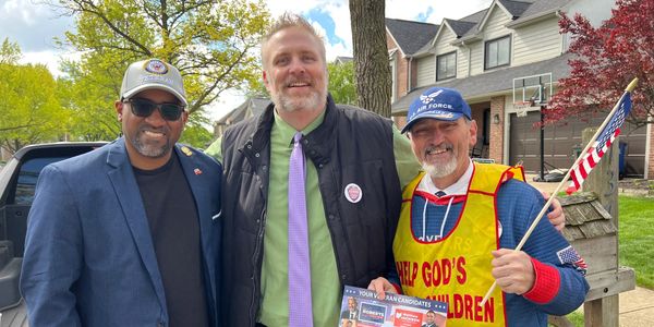 Three men smiling together outdoors in a suburban neighborhood.